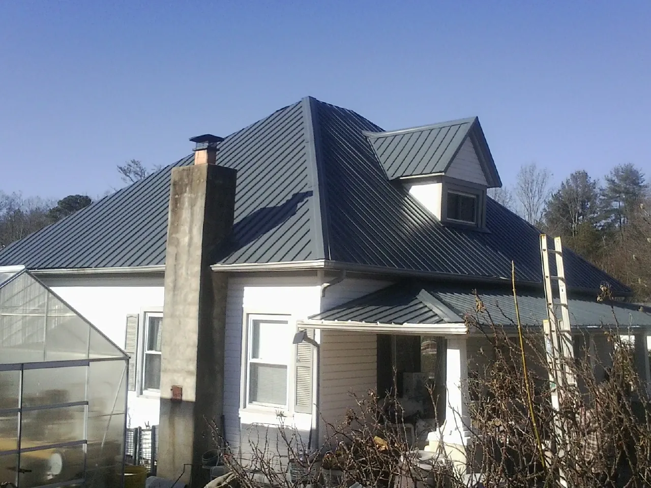 Dark blue standing seam metal roof on a white farmhouse with dormer — Slate & Tile Roof Repair by Roofing Brothers in Dillonvale
