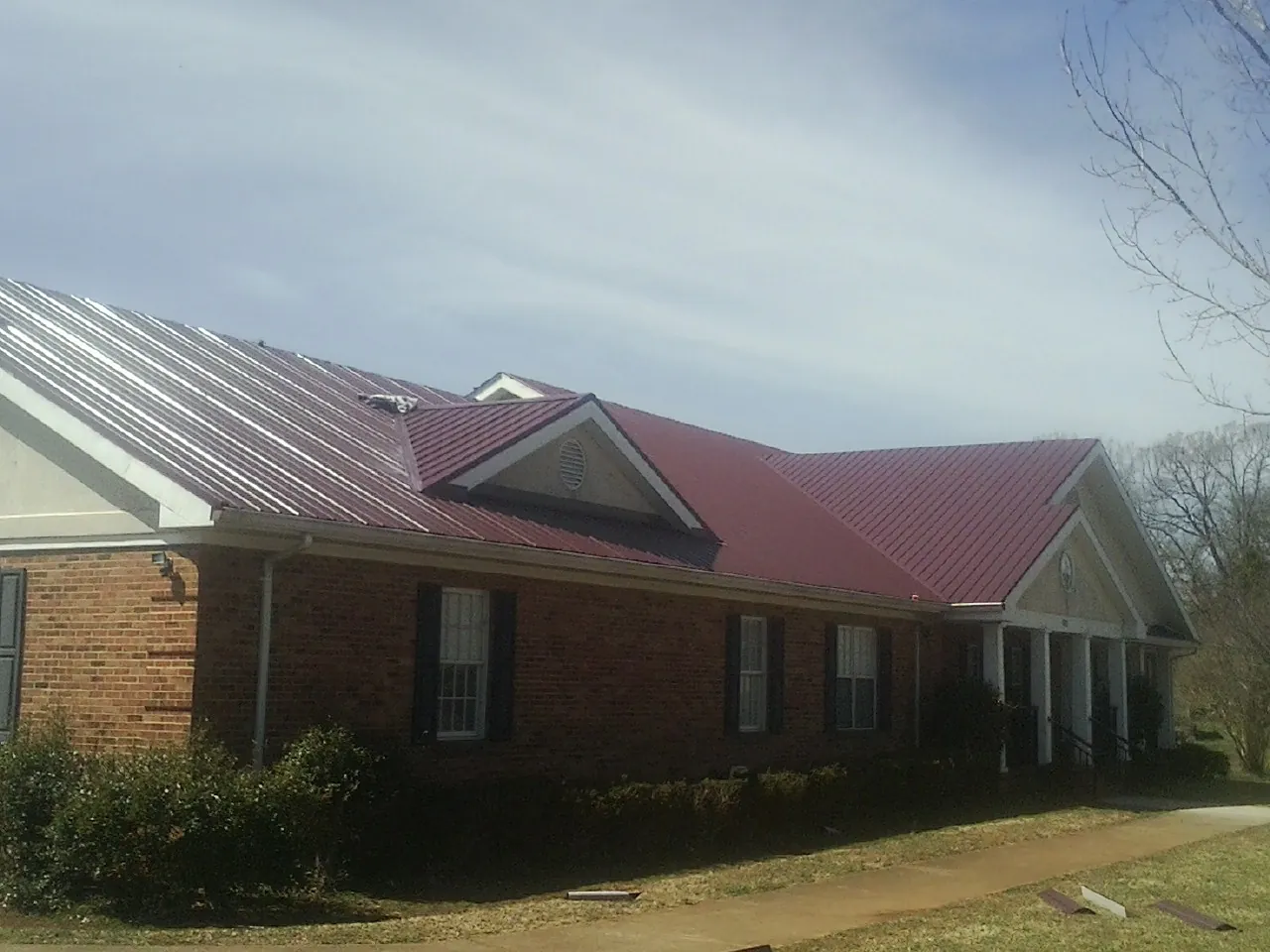 Red metal roof with gabled entries on a long brick building, from a Hail Damage Roof Repair job in Dillonvale