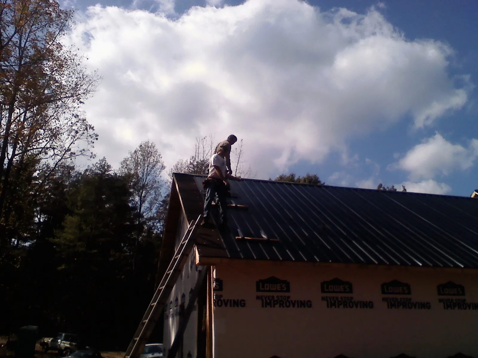 Roofer fastening dark metal panels high against a cloudy sky, from a Roof Inspection job in Dillonvale