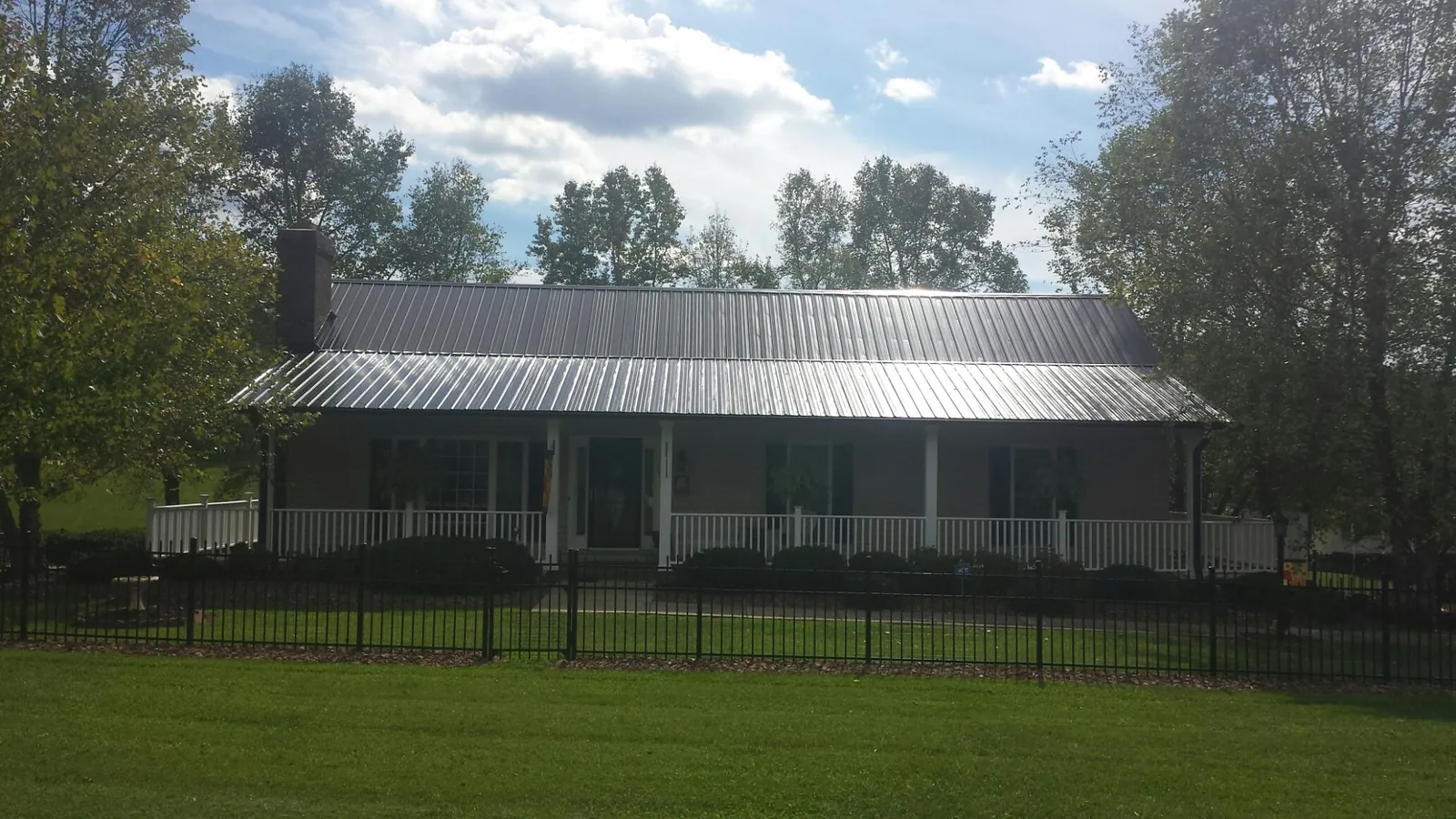 Gray metal roof on a brick ranch with a full width front porch — Gutter Guard Installation work by our crew in Dillonvale